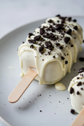 A close-up of a white chocolate-covered cakesicle with cookie crumble topping on a light gray plate.